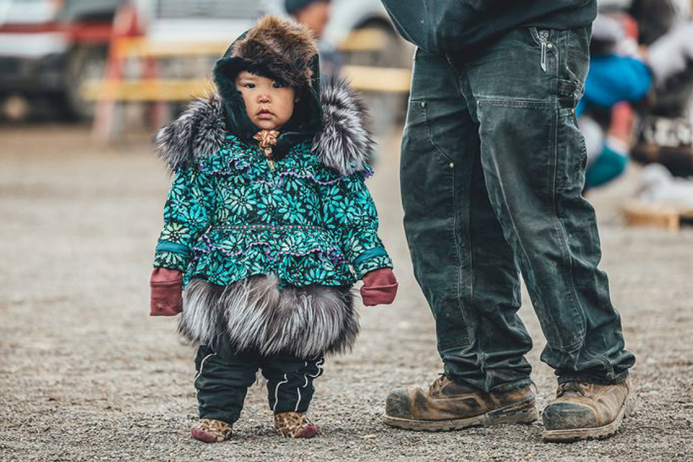 Toddler in traditional fur attire with green flower patterned coat