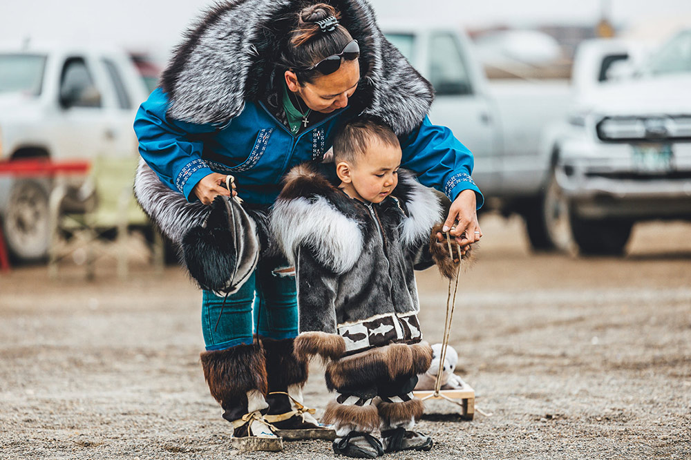 Toddler in gray traditional fur attire with his mom
